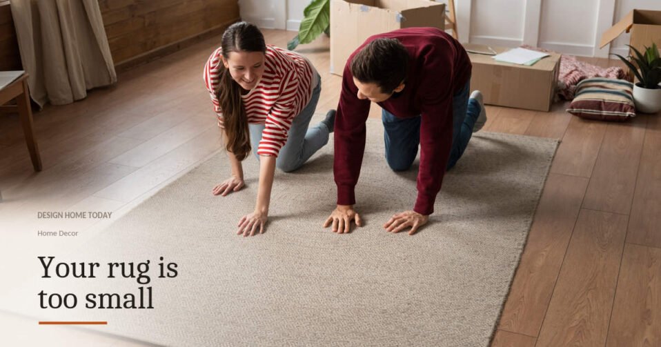 A couple kneeling to flatten a large woven rug in a room with moving boxes